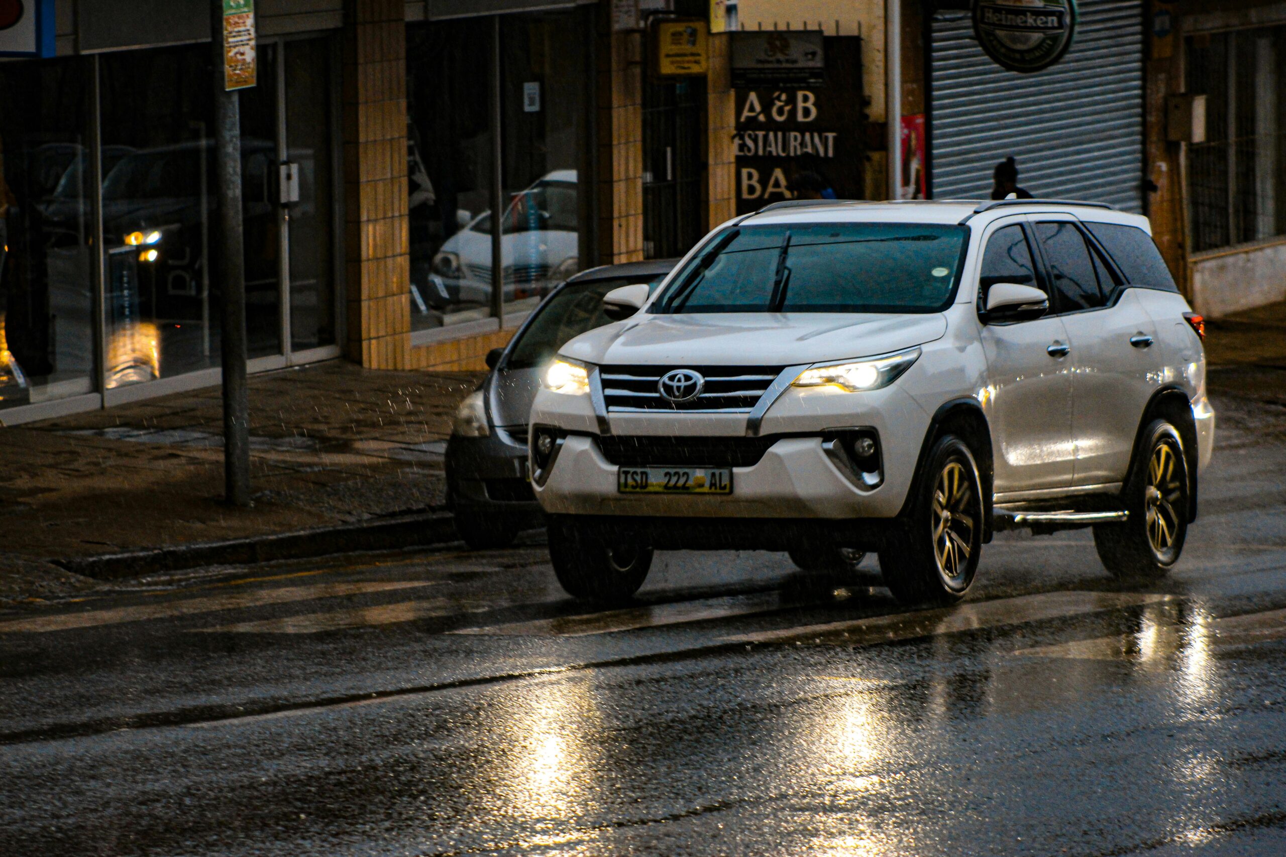 A white Toyota SUV driving on a wet city street at night, reflecting urban lights.